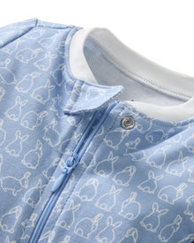 The Baby's Pima Romper in Hoppy Days Blue features a blue footed design with white cuffs, a white collar, white-outlined bunny pattern, and a diagonal zipper from neck to leg.