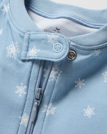 The Baby's Pima Romper in Periwinkle Wonderland is a light blue onesie with long sleeves, covered feet, white snowflake pattern, diagonal zipper from neckline to left ankle, and a small fabric snap at the neck.