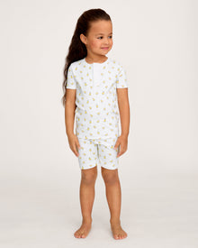 A young child with long brown hair smiles while wearing the Kid's Pima Snug Fit Short Set in Tres Chick, standing against a plain light background.