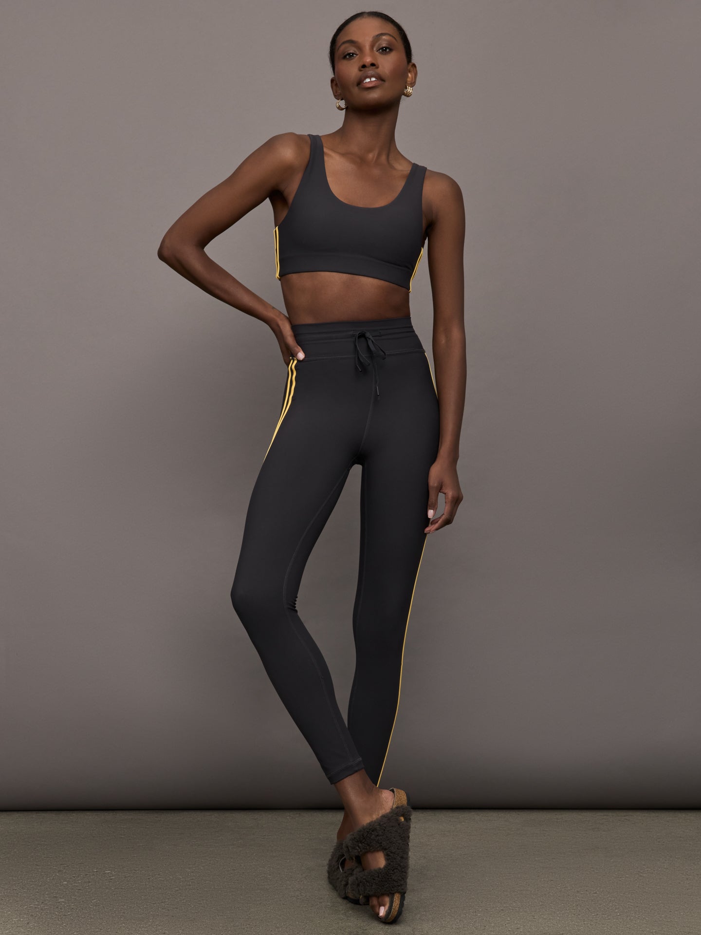 Model is wearing a black scoopneck sports bra with yellow striped sides. 