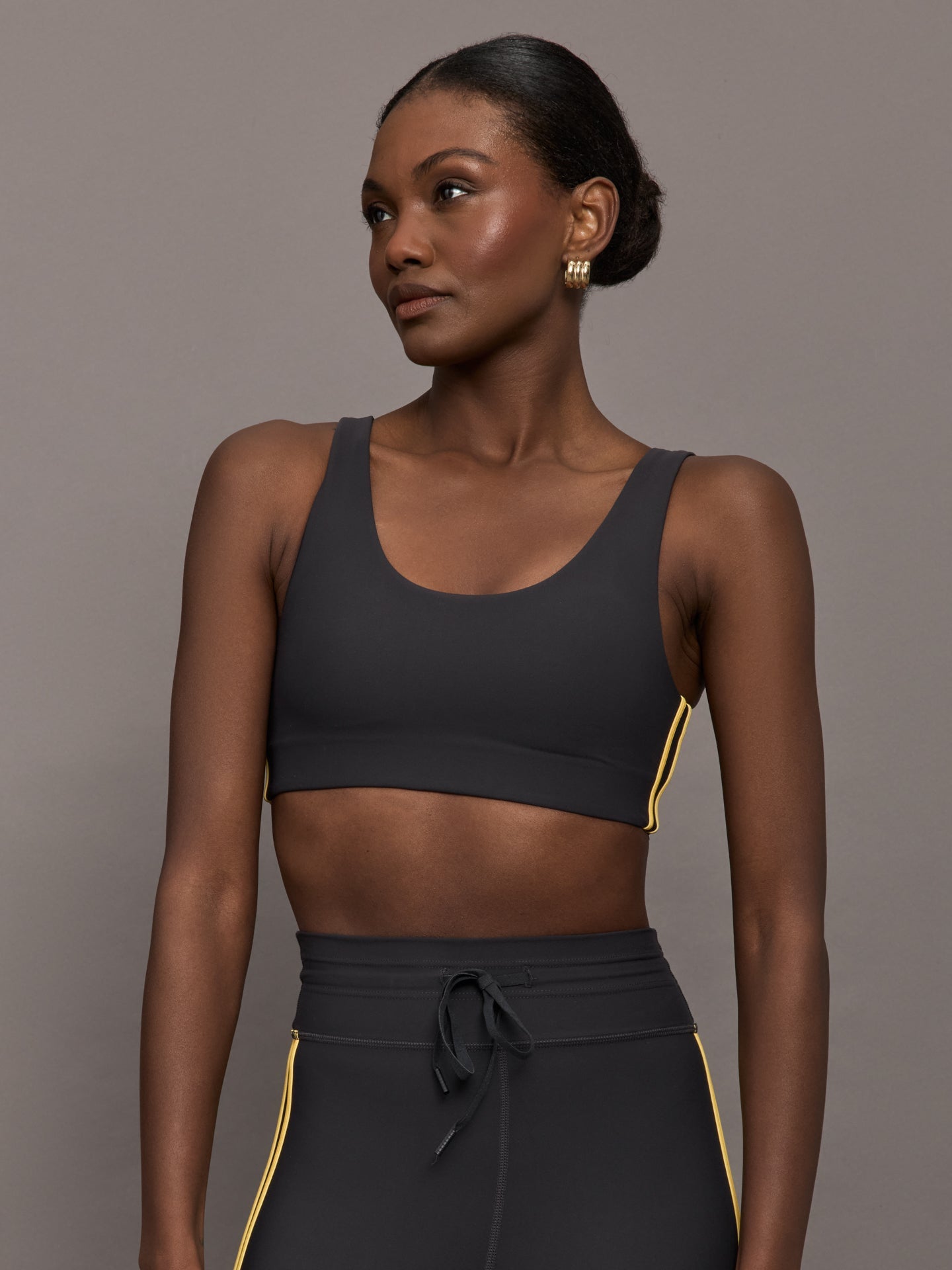 Model is wearing a black scoopneck sports bra with yellow striped sides. 