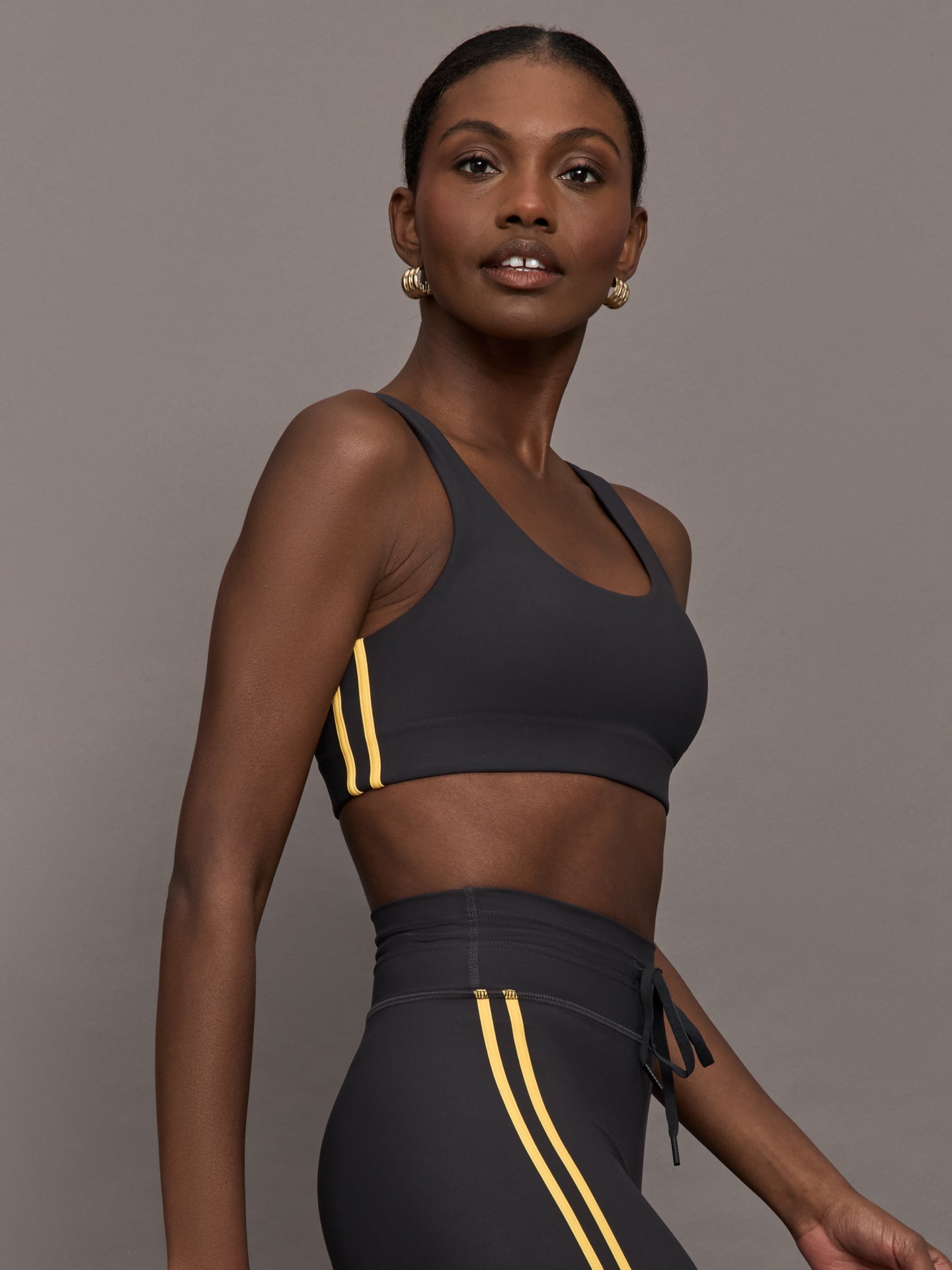 Model is wearing a black scoopneck sports bra with yellow striped sides. 