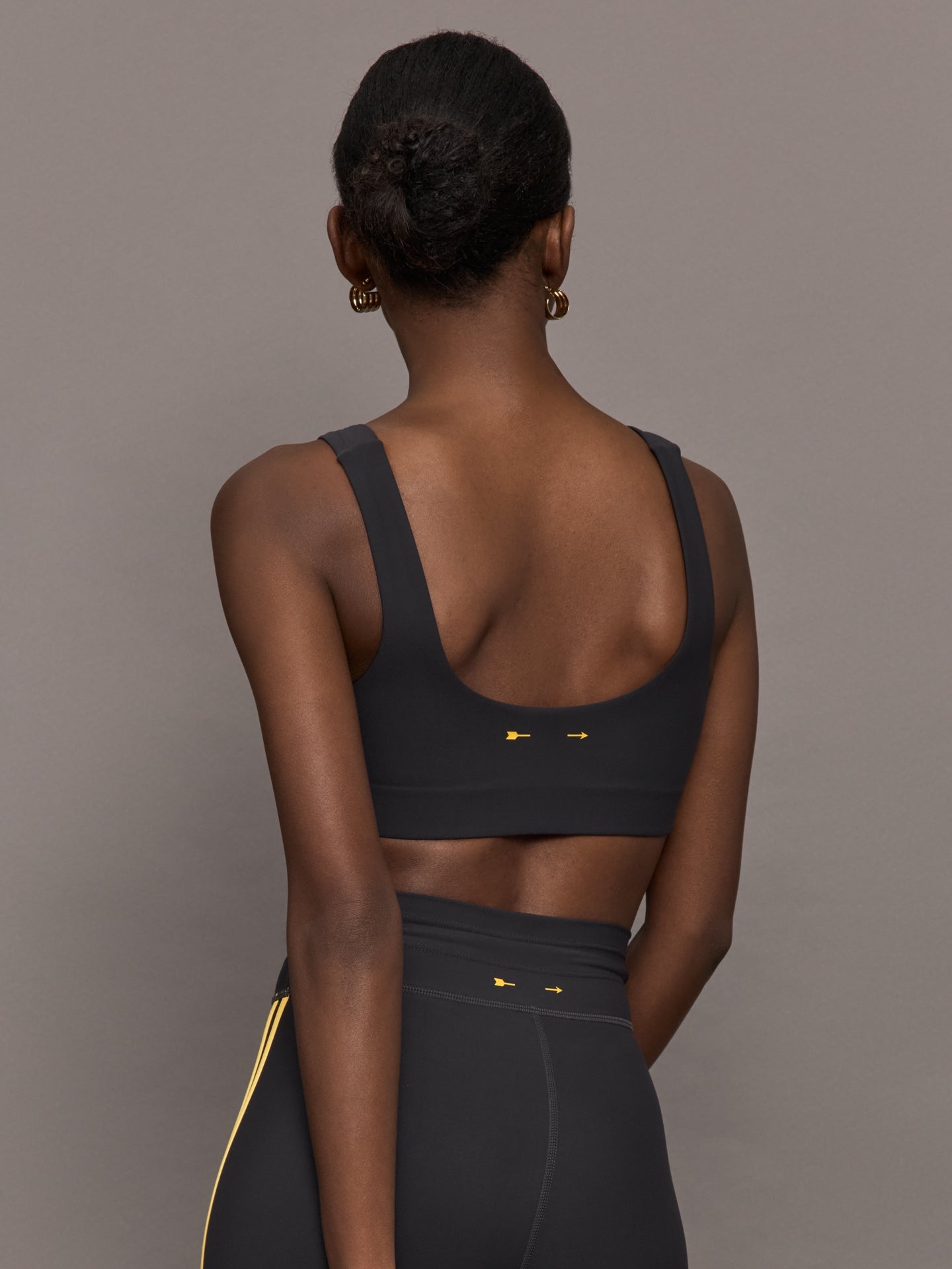 Model is wearing a black scoopneck sports bra with yellow striped sides. 