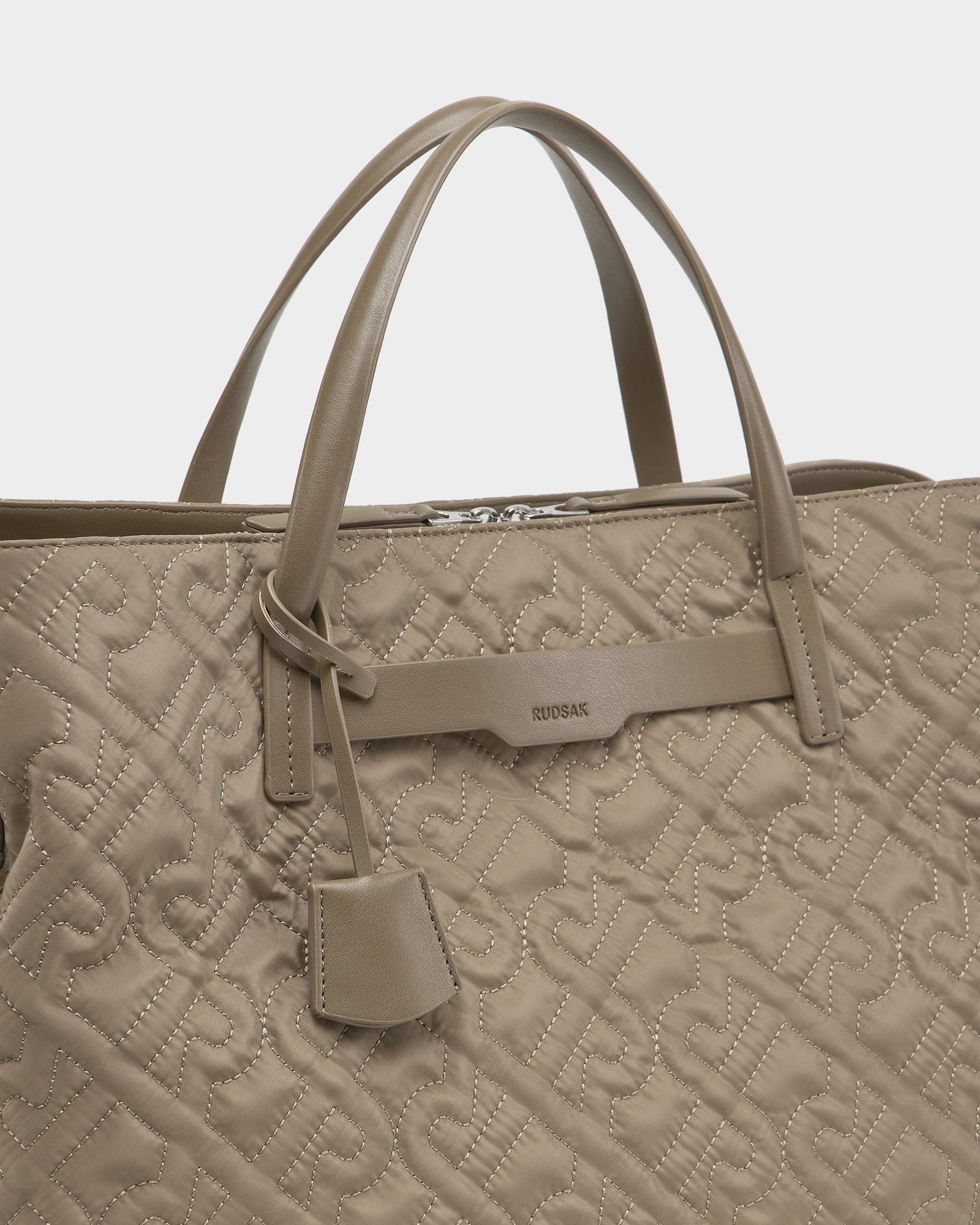 The ASMINE - L325005 Almond by Rudsak is a taupe quilted tote with top handles, featuring a repeating “RS” monogram, an attached leather tag, and the Rudsak logo on the front—an elegant accessory for any outfit.