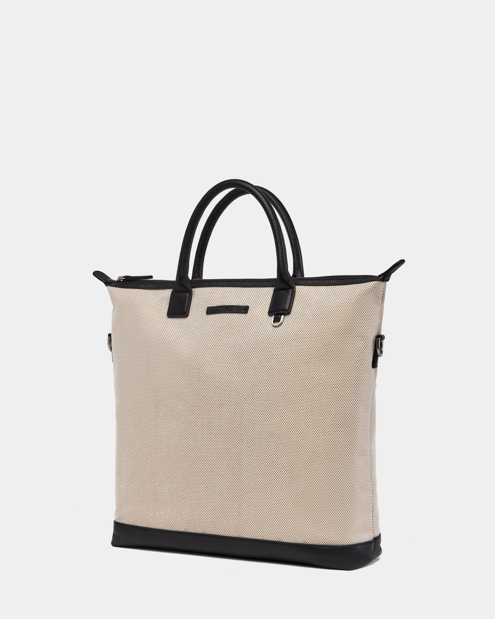 The Rudsak DEXTER - 9324513 Vanilla is a unisex beige canvas tote bag with black leather handles, trim, and base. Featuring a simple, structured design, its shown against a plain white background.