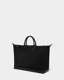 The DUBLIN - 9324514 Black by Rudsak is a sleek, black weekender tote with two short handles, silver-tone hardware, and a structured rectangular shape, shown against a plain light gray background.