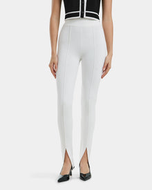 A woman wears Rudsak’s MATHILDA - 8524515 Iceland high-waisted white ankle-slit leggings with front center seams and split hems, styled with black pointed-toe heels and a sleeveless black top.
