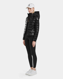 A person wearing the MELISSA - 8121000 BLACK women’s puffer jacket with RDS certified down, black leggings, white sneakers, and a white baseball cap stands against a plain light background, facing forward with a neutral expression.