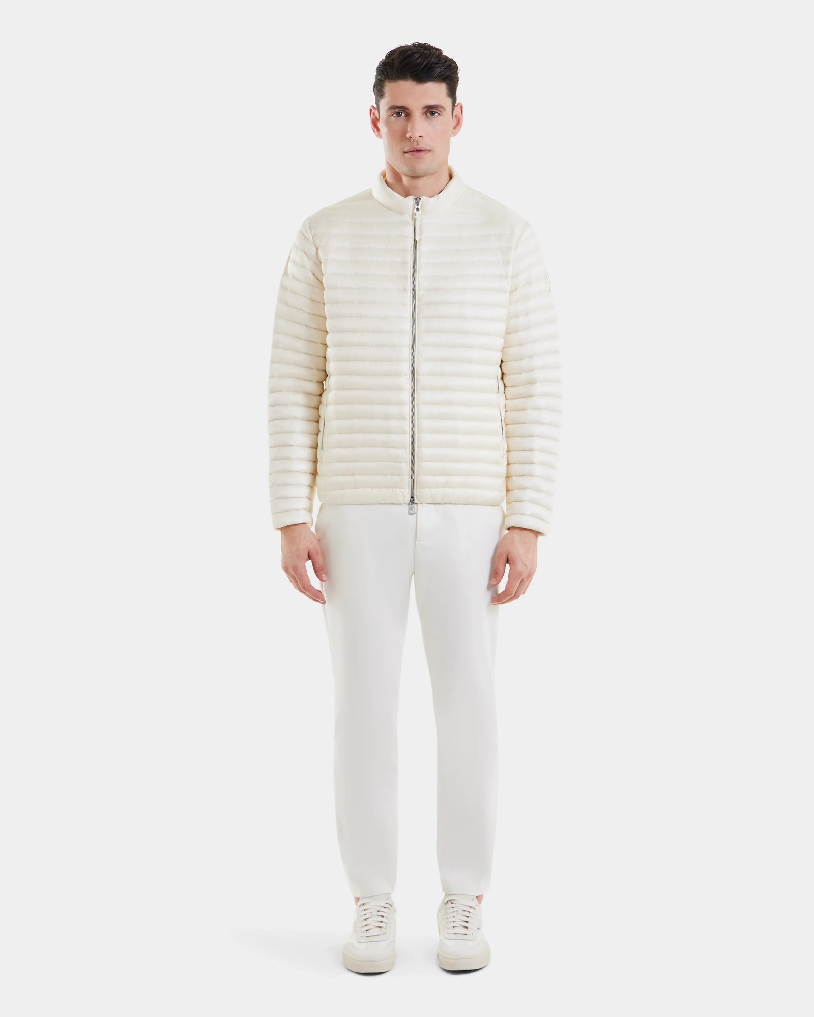 A man stands facing forward, wearing the REYMOND - M125013 Iceland off-white quilted men’s down jacket by Rudsak, paired with matching white pants and white sneakers against a plain white background.