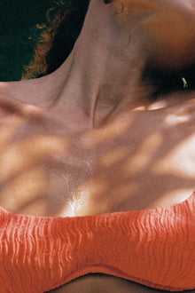 Tangerine textured bikini top worn on model against dark water background.