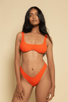 Tangerine bikini top with textured fabric and wide shoulder straps on a model against a neutral background.