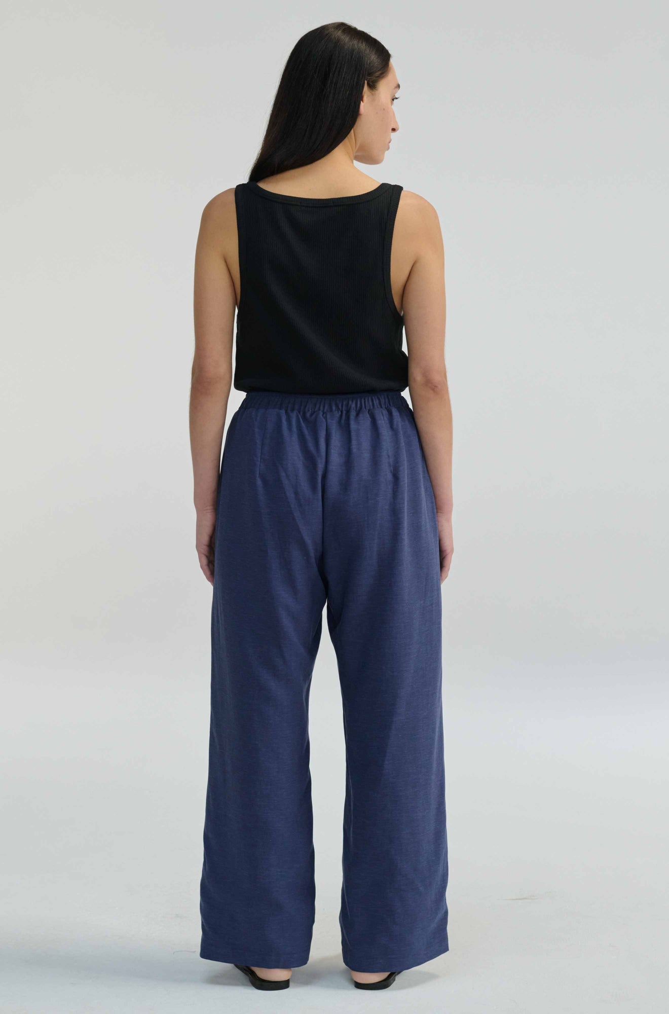 Woman wearing a black sleeveless top and blue pants on a light gray background