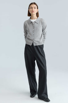 Person wearing a gray cardigan and black pants on a light gray background