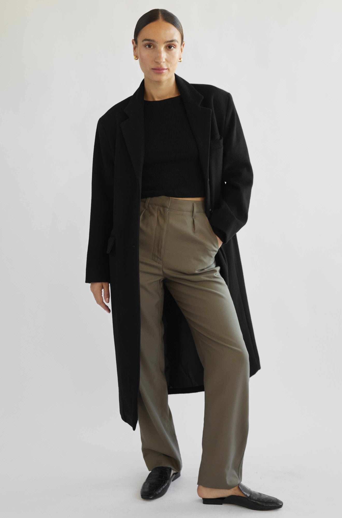 Person wearing a black coat, black top, and beige pants on a white background