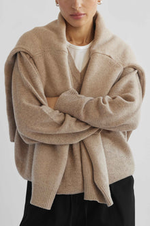 Person wearing a beige cardigan over a white shirt on a light gray background