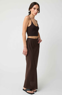 Woman wearing a brown sleeveless top and long skirt on a white background