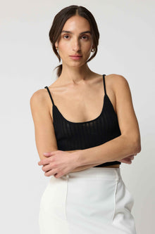 Woman wearing a black top and white pants against a plain background