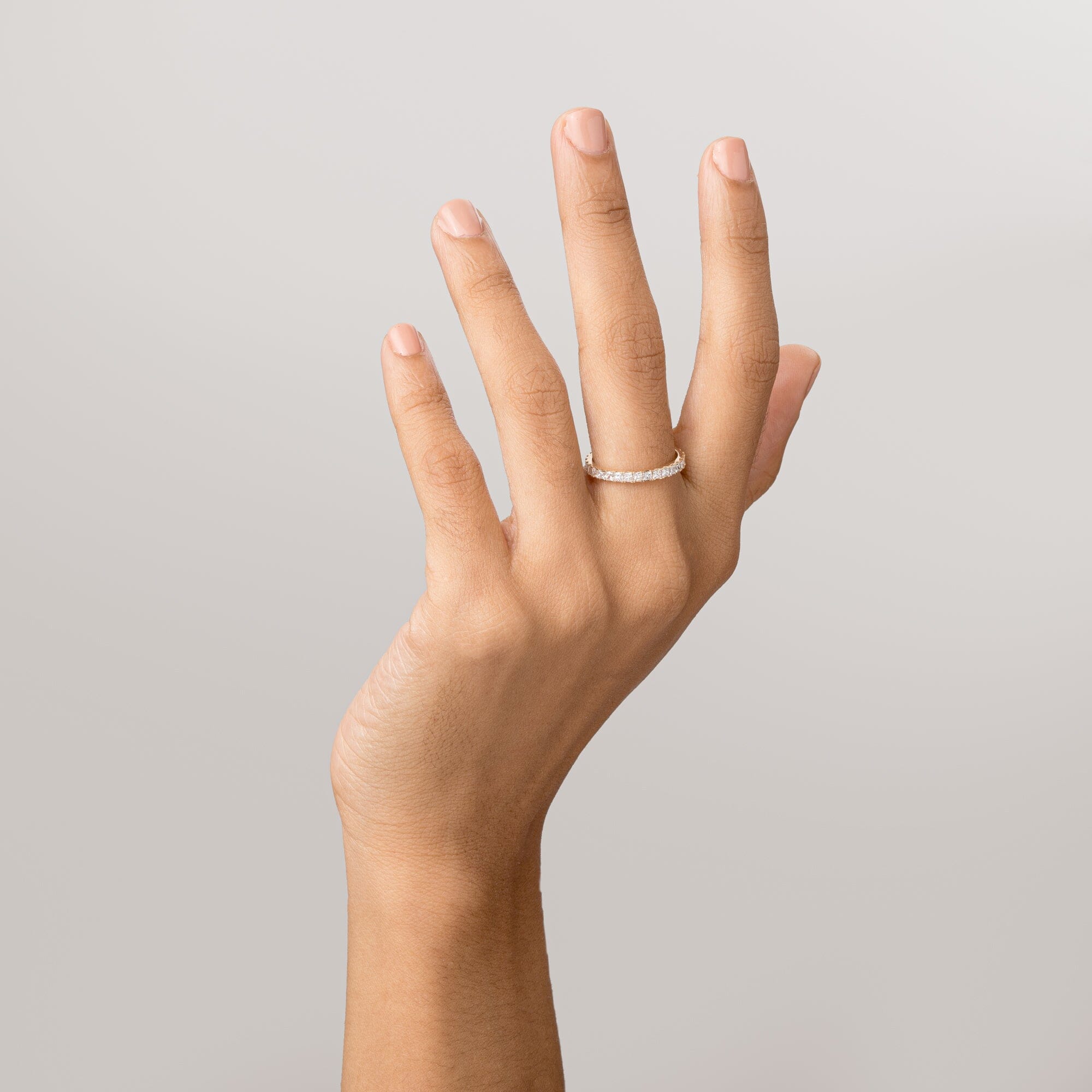 Model Close-up of a woman's hand with fingers extended upward, wearing a gold diamond eternity ring against a plain light background