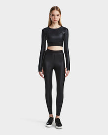 A woman faces forward wearing the Rudsak LORA - 8524026 Black fitted long sleeve top with high-waisted black leggings and sneakers, set against a plain light background.