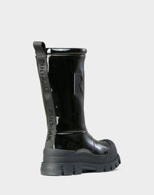 The KRISTAL HI - 8222510 BLACK by Rudsak is a shiny black high-gloss winter boot with chunky grip soles, embossed Rudsak branding on the pull tab and heel, and a large R on the side, shown from the back and side against a light background.