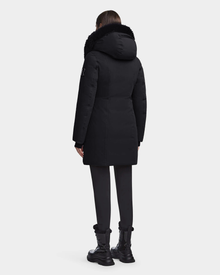 A person wearing the Rudsak MAIA M - 8123582 Black womens down parka with a faux fur hood, black pants, and black boots stands facing away from the camera against a plain white background.