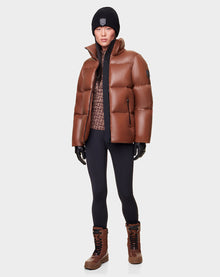 Wearing the RUDSAK DORA - 8122547 COHIBA brown down puffer, a person pairs it with a patterned sweater, black leggings, brown winter boots, black gloves, and a black beanie against a plain light background.