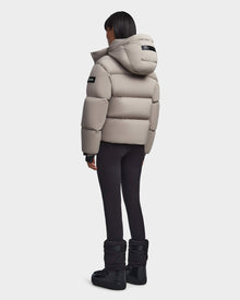 A person stands facing away, wearing the Rudsak MAVE M - 8123572 Cement down puffer jacket, black leggings, and black winter boots against a plain white background.