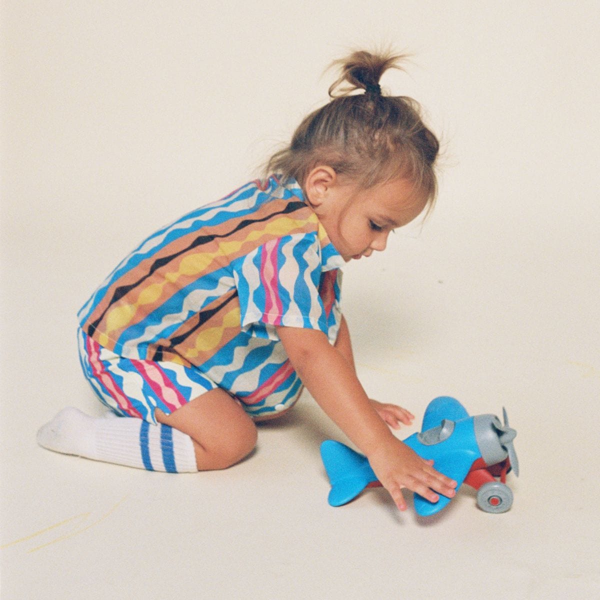 Child wearing short-sleeve button-down shirt with abstract wavy stripes in blue, pink, yellow, and white.