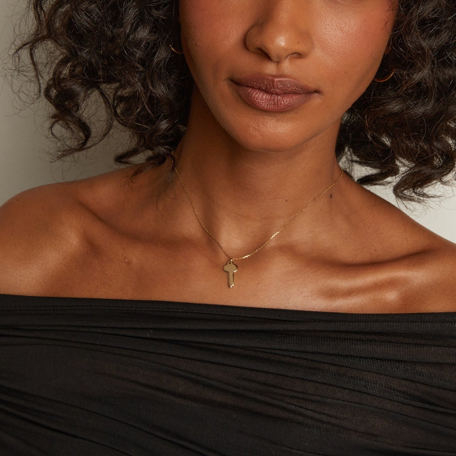 Model. Woman wearing a gold necklace with a pendant against a neutral background