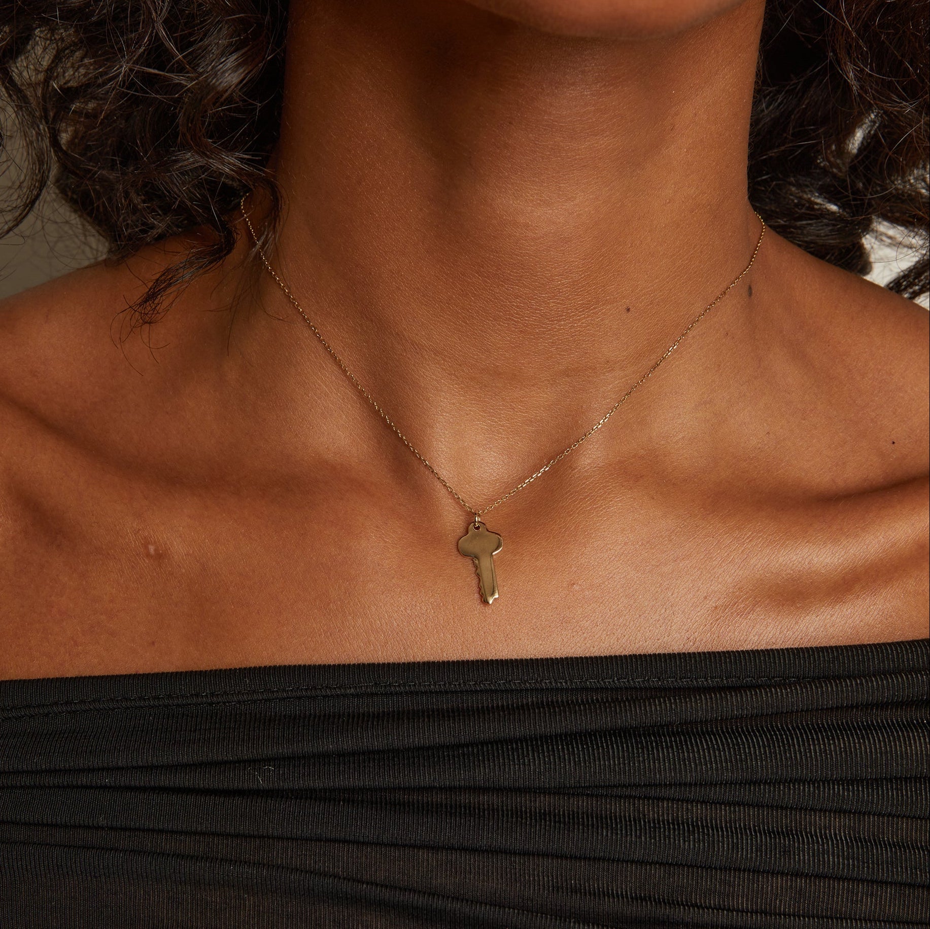 Model. Necklace with a key pendant worn by a person in a black top.