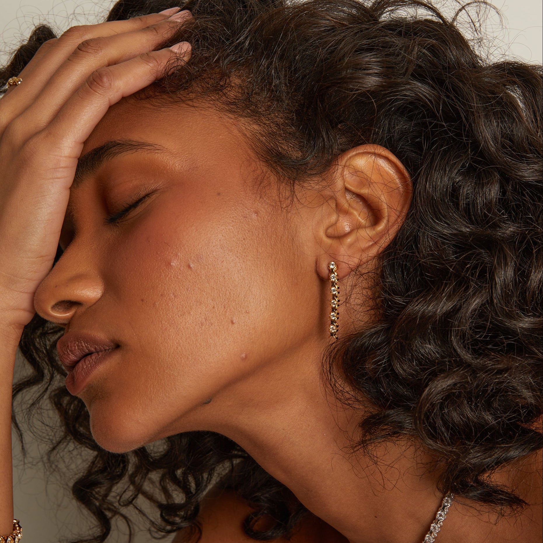 Model. Close-up of a woman with curly hair wearing earrings, with a neutral background