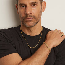 Model. Man wearing a black shirt with gold jewelry against a plain background