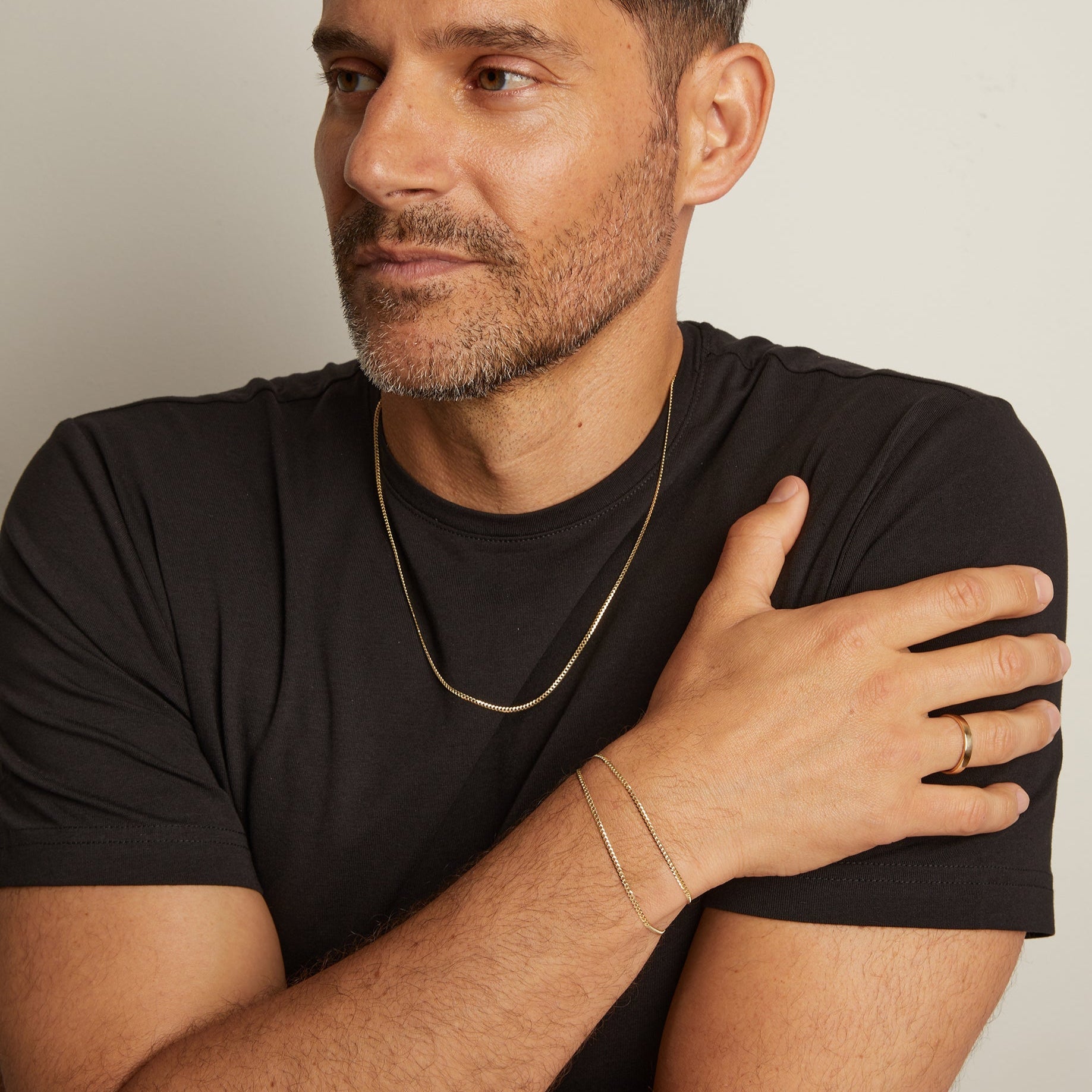 Man wearing a black t-shirt with jewelry on a neutral background
