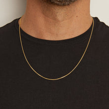 Model. Man wearing a gold chain necklace against a neutral background
