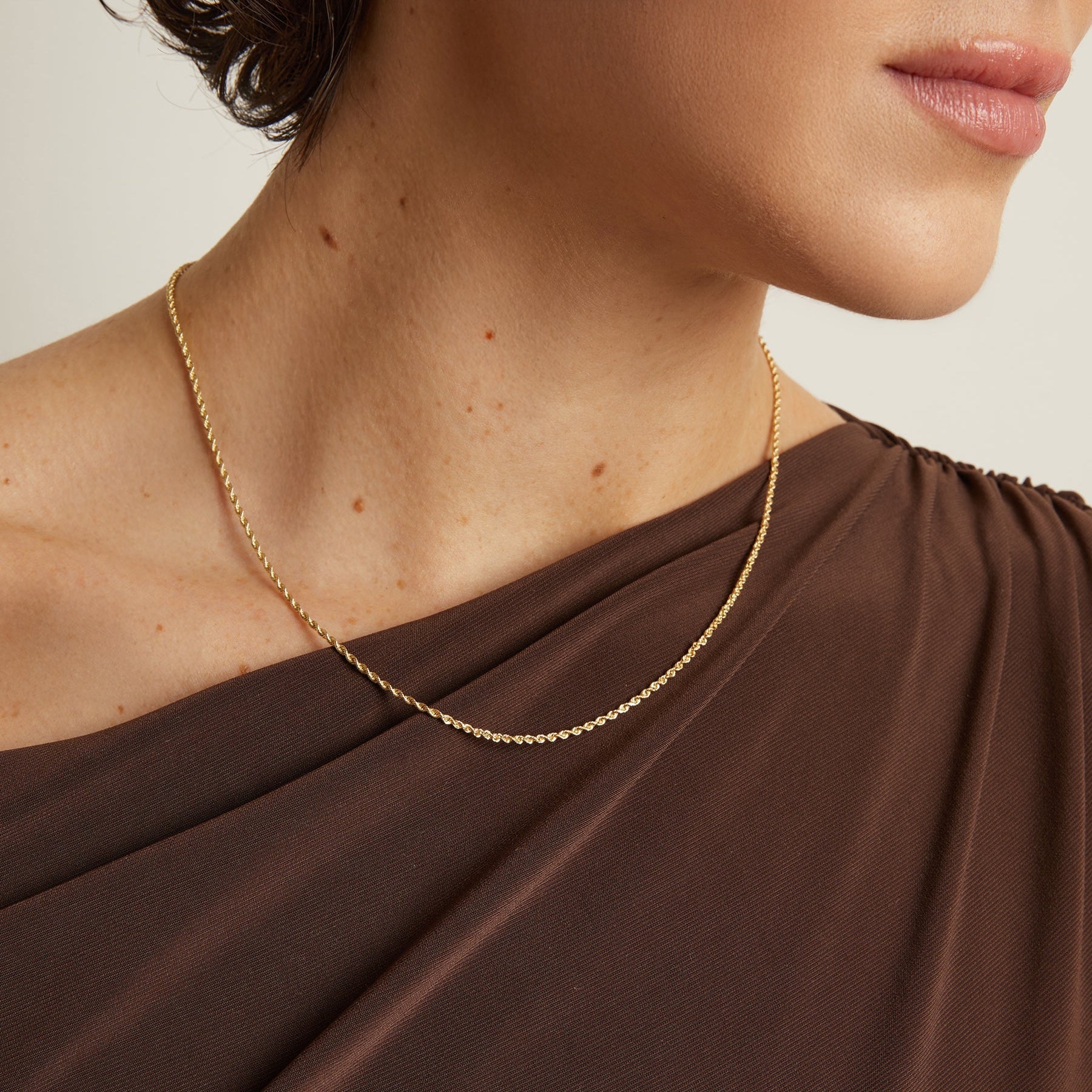 Model. Gold necklace on a person wearing a brown garment