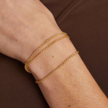 Model. Gold bracelet on a wrist against a brown background