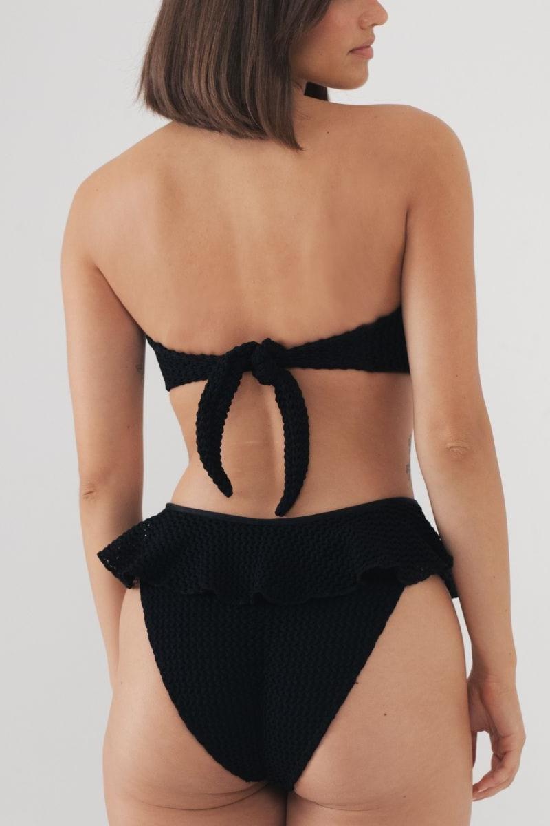 Black crochet bikini bottom with ruffle waistband detail, shown from back view on model.