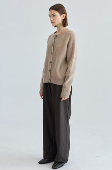Person wearing a beige cardigan and dark pants on a white background