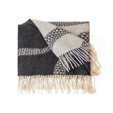 A folded woven throw blanket with cream fringe, featuring a geometric pattern in black, gray, and cream on a white background.