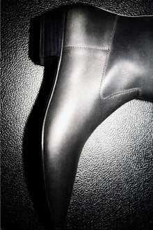 Black leather riding boot with stitched seams and smooth finish, shown in profile against textured background.