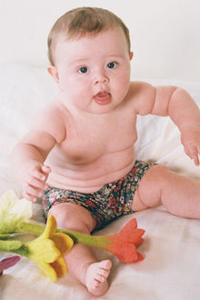 Infant wearing multicolored floral print swim trunk with dark base and red, pink, and teal flowers.