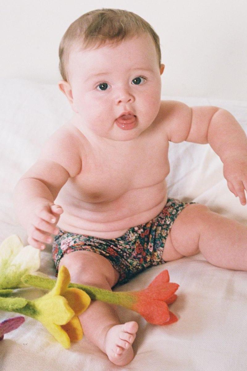 Infant wearing multicolored floral print swim trunk with dark base and red, pink, and teal flowers.