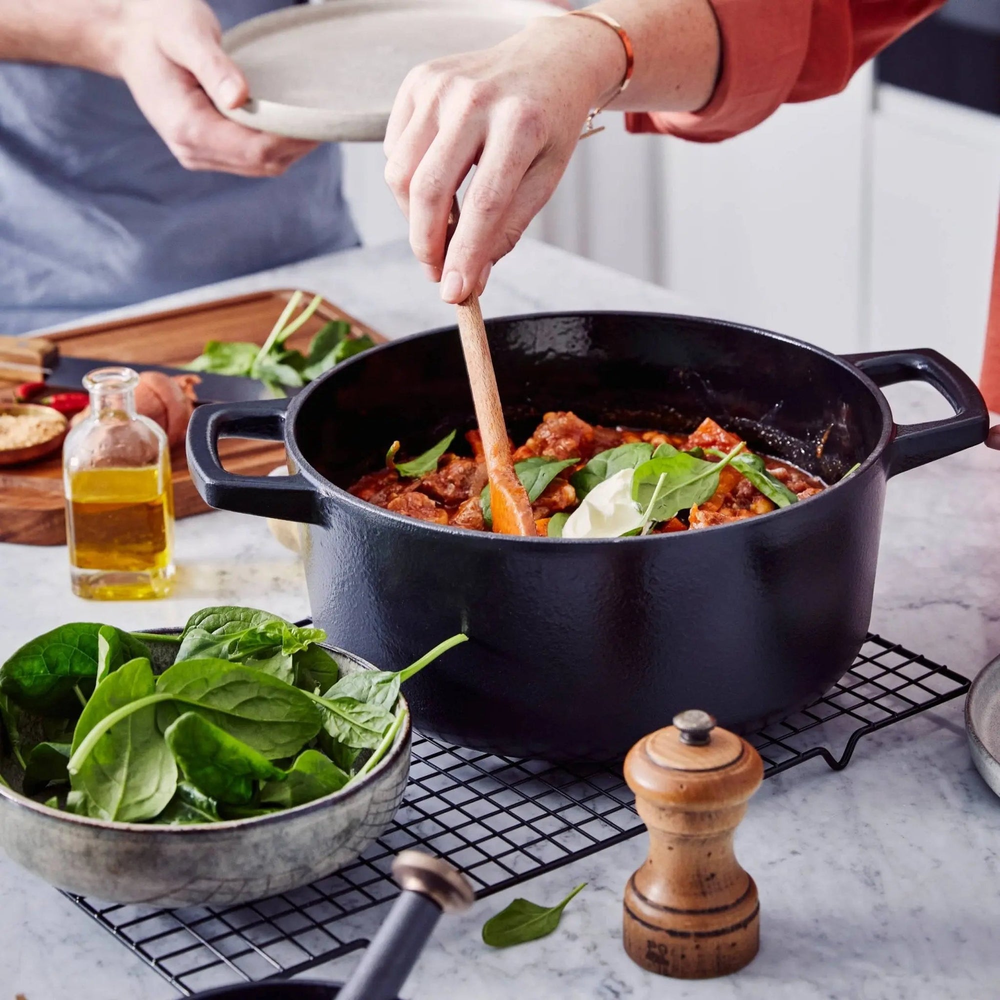 Black Dutch oven filled with stew, spinach, and sour cream, being stirred in a modern kitchen.