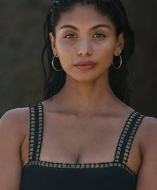 A woman wearing black a one-piece swimsuit with crochet trim details around the neck and shoulders standing on the beach
