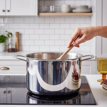 Stainless steel stock pot on induction cooktop with hand stirring wooden spoon in modern kitchen